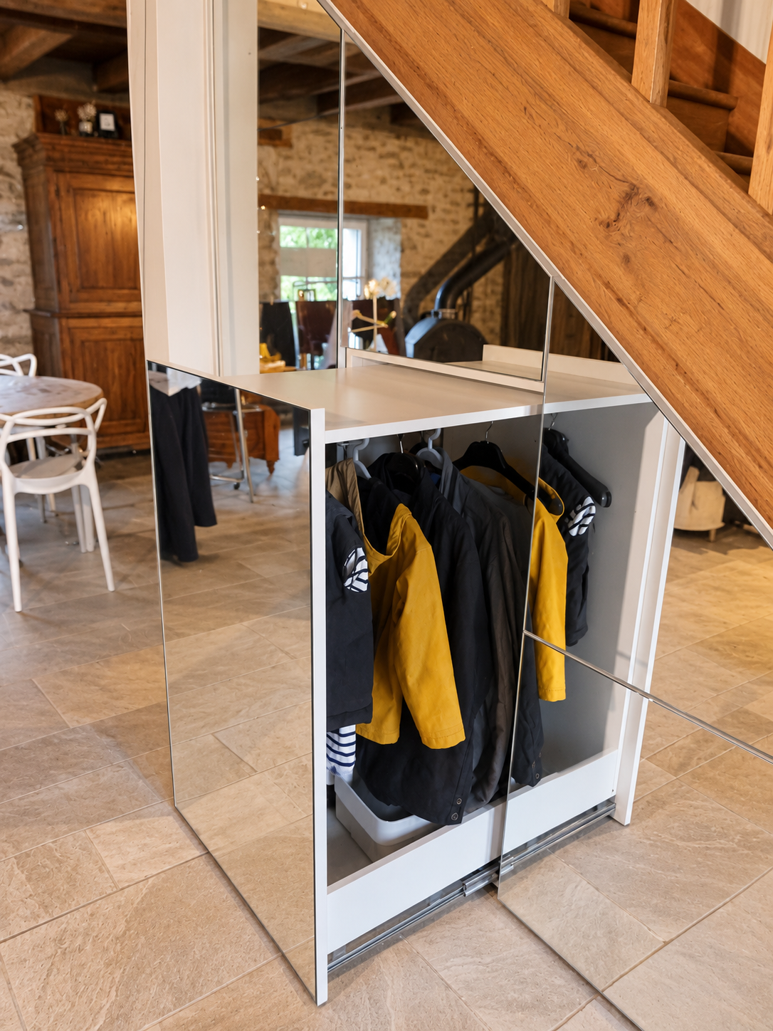 Penderie sous escalier ouverte avec vêtements et façade miroir